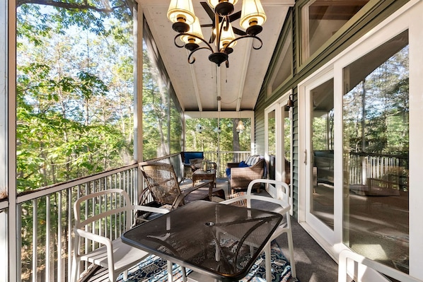 A covered porch with outdoor furniture, a table, and chairs, overlooking a forested area.