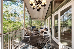 A covered porch with outdoor furniture, a table, and chairs, overlooking a forested area.