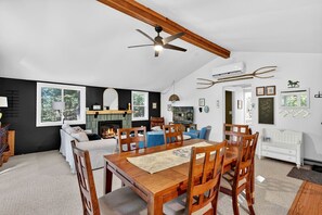 A spacious living area with a fireplace, a dining table with chairs, a ceiling fan, and a large window.