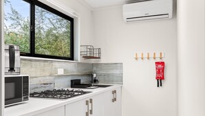 A modern kitchen with white cabinets, a gas stove, a microwave, and a window overlooking greenery. - Bright 1-bed Apartment With Garden Views (Nowra)