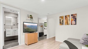 A modern living room with a grey sofa, a television, and artwork on the wall. - Bright 1-bed Apartment With Garden Views (Nowra)
