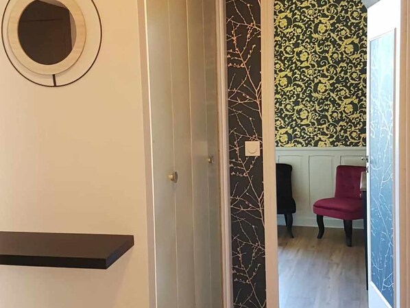 Una habitación con un espejo circular, un papel tapiz con diseño negro y dorado, una silla roja y suelo de madera.