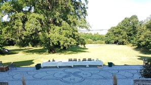 A covered outdoor seating area with a table set up for dining, surrounded by trees and a view of a body of water.