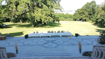 A covered outdoor seating area with a table set up for dining, surrounded by trees and a view of a body of water.