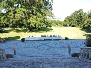 Un área de estar al aire libre con techo, con una mesa lista para comer, rodeada de árboles y vista a un cuerpo de agua.