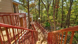 A wooden staircase with red railings leading to a house surrounded by trees.
