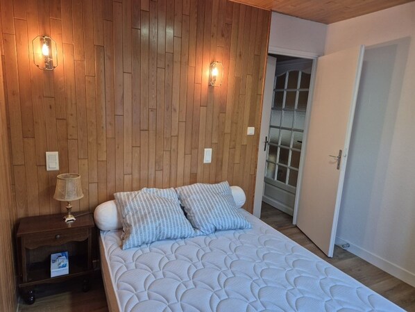 A bedroom with a wooden headboard, a bed with patterned bedding, a nightstand with a lamp, and a door leading to a bathroom.