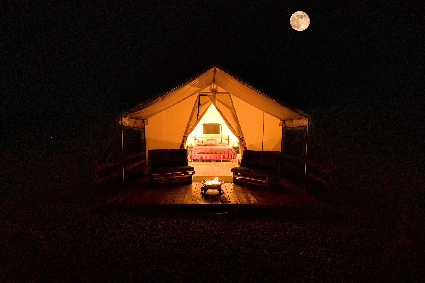 A tent with a bed, a table, and a fire pit.