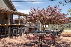 Un patio al aire libre con una parrilla, taburetes de bar y mesas.