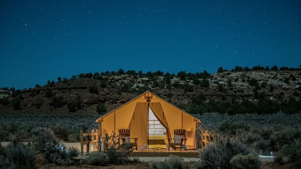 A tent-like structure with a central entrance, surrounded by sparse vegetation, set against a night sky. - Safari Tent Adventure in Kanab, Utah: A Unique Glamping Experience (Kanab)