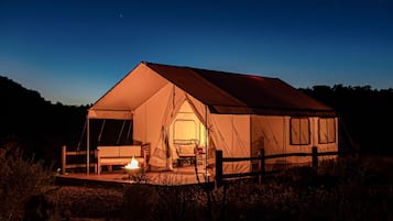A large tent with a fire inside, a bench, and a chair outside.