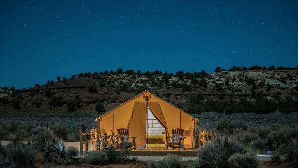 A tent-like structure with a central entrance, surrounded by sparse vegetation, set against a night sky.