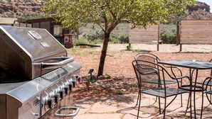 A stainless steel grill, outdoor seating with chairs and a table, and a tree in a landscaped area. - Safari Tent Adventure in Kanab, Utah: A Unique Glamping Experience (Kanab)