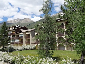 Un hôtel doté de nombreux balcons, d’un jardin agrémenté de fleurs blanches et offrant une vue sur les montagnes en arrière-plan.