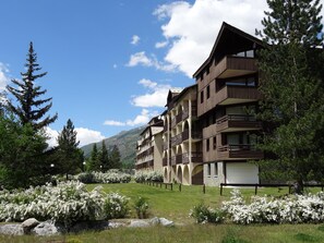 A multi-story hotel with balconies, surrounded by greenery and flowering bushes. - Comfortable studio, shuttle to slopes, parking (La Salle-les-Alpes)