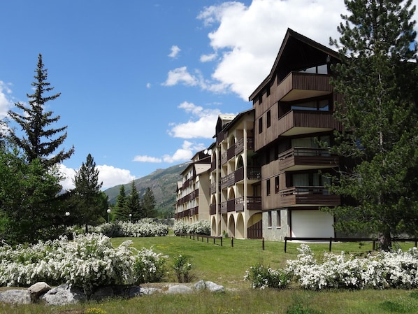 A multi-story hotel with balconies, surrounded by greenery and flowering bushes.