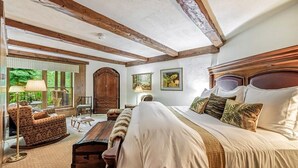 Ein Schlafzimmer mit einem großen Bett, Holzbalken, einem Schminktisch, einem Stuhl und einem Fenster mit Blick ins Grüne.
