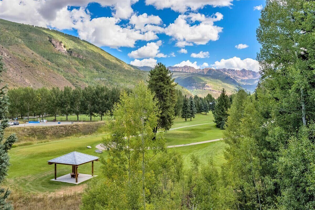 Golfkenttä, jossa on katettu lepopaikka, ja jota ympäröivät puut ja taustalla kohoavat vuoret.