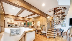 Ein geräumiger Wohnbereich mit Holztreppe, Holzbalken an der Decke und einem Essbereich mit Stühlen und Tisch.