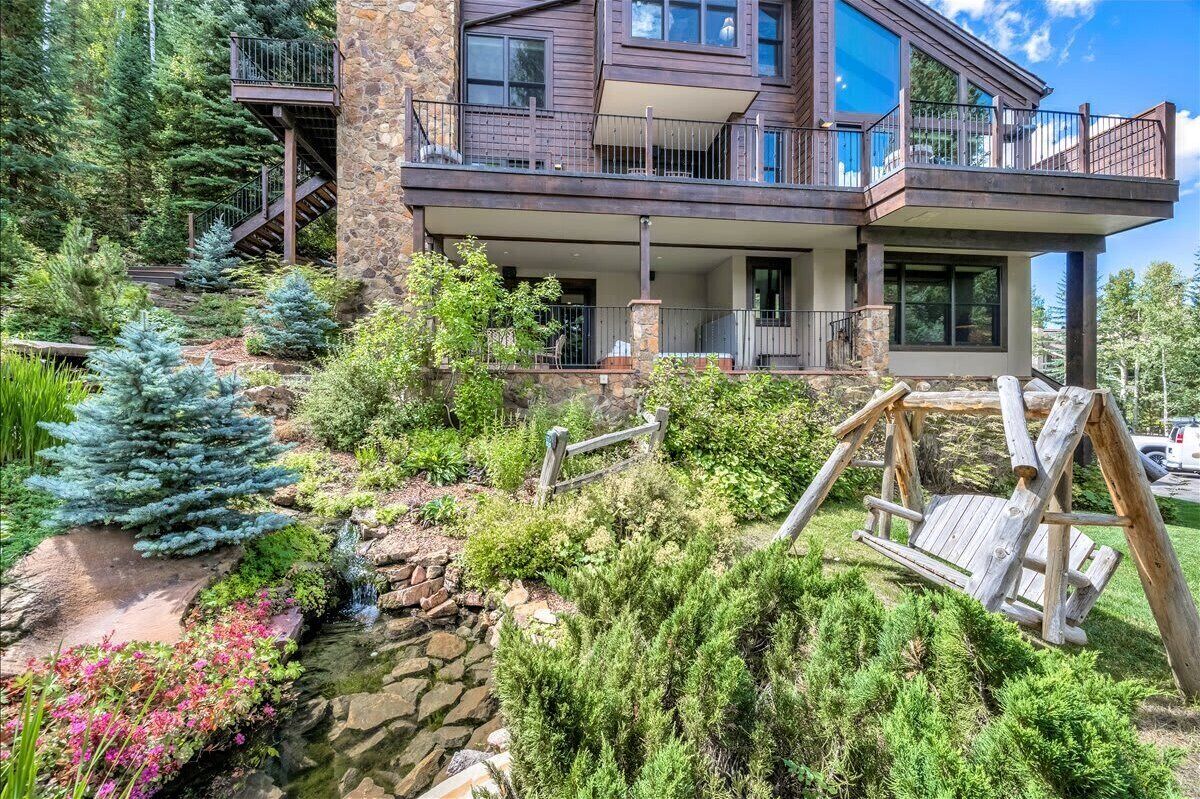 Ein zweigeschossiges Haus mit einer Steinfassade, einem Balkon und einem kleinen Garten mit Teich und Schaukel.