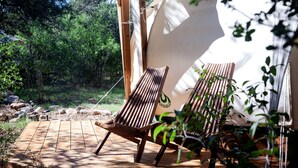 Una terraza de madera con dos sillones de descanso, una tienda de campaña y un entorno natural.