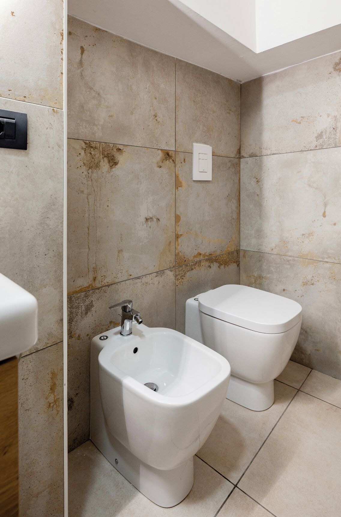 A bathroom with a bidet, a toilet, and a wall-mounted light switch.