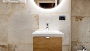 A modern bathroom with a round mirror, white sink, wooden cabinet, and a bathtub. - Antrum Loft, eaperience with Jacuzzi (Salerno)