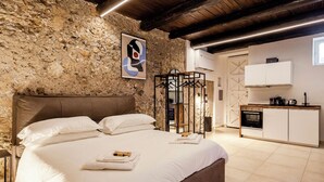 A bedroom with a stone wall, a bed with white linens, a wooden headboard, a black metal wardrobe, and a kitchenette with a stove. - Antrum Loft, eaperience with Jacuzzi (Salerno)