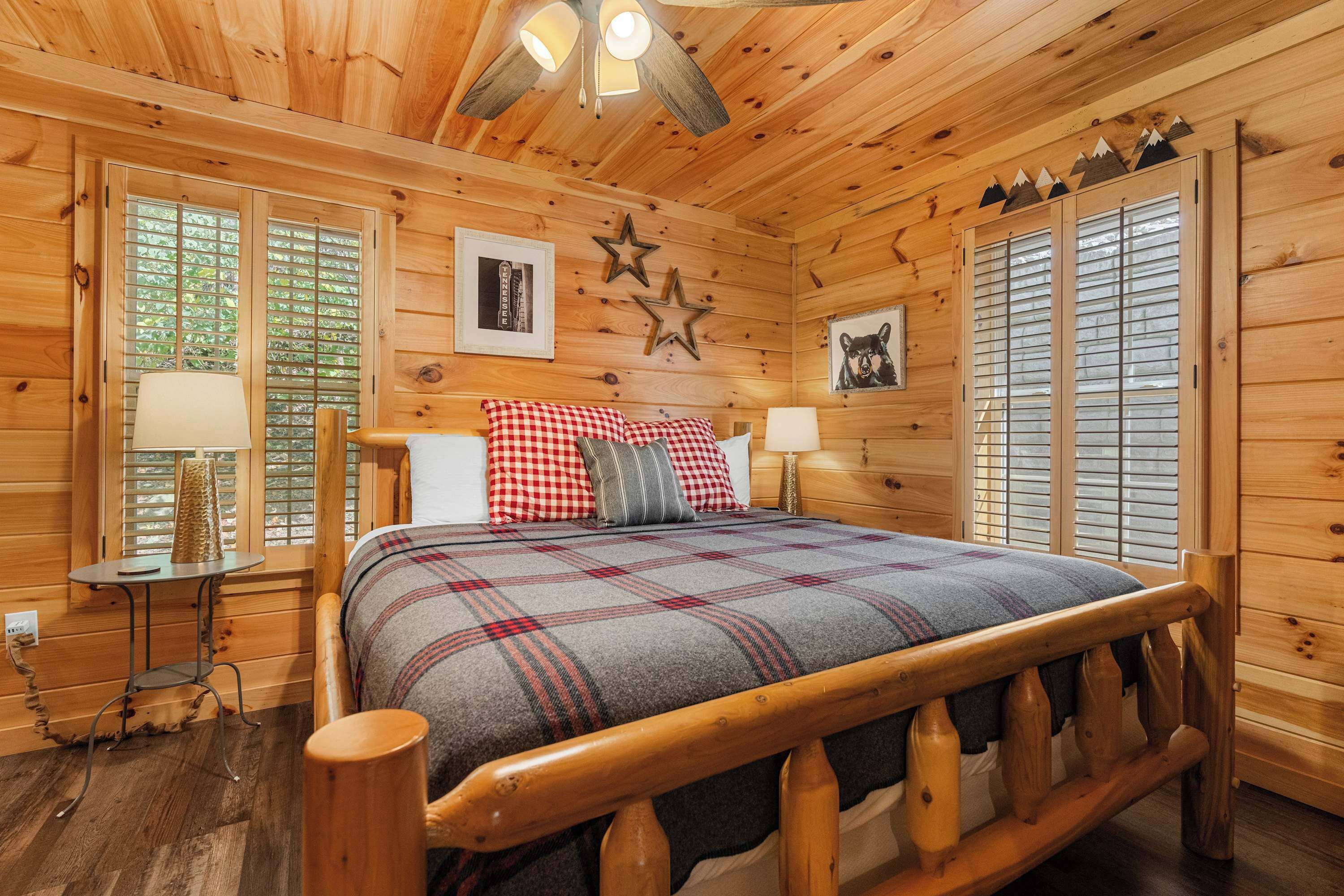 A wooden cabin bedroom with a bed, two bedside tables, a lamp, and a window with shutters.