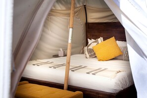 A tented room with a bed, pillows, a bedside table, and a small stool.