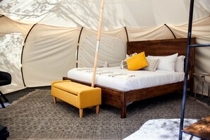 A tented room with a bed, a yellow bench, and a wooden headboard.
