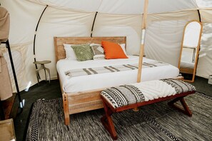 A tented room with a wooden bed, pillows, a bench, and a mirror. - Romantic Escapes to Spicewood, Texas in this Charming Bell Tent for Two (Spicewood)