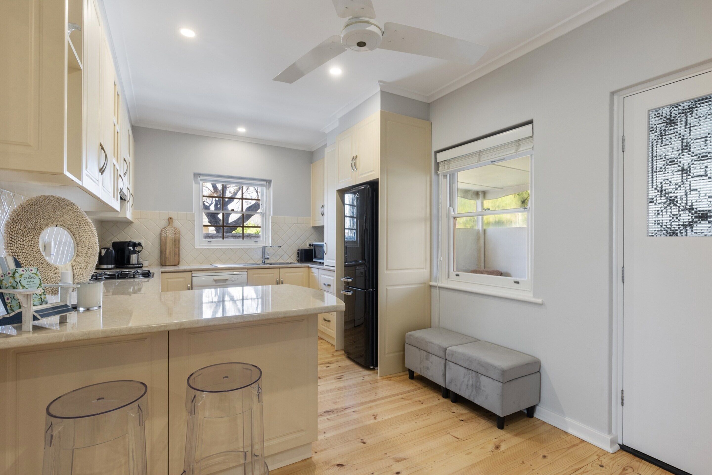 A modern kitchen with a central island, bar stools, a built-in oven, and a window overlooking the garden.