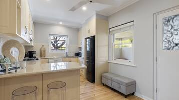 A modern kitchen with a central island, bar stools, a built-in oven, and a window overlooking the garden.