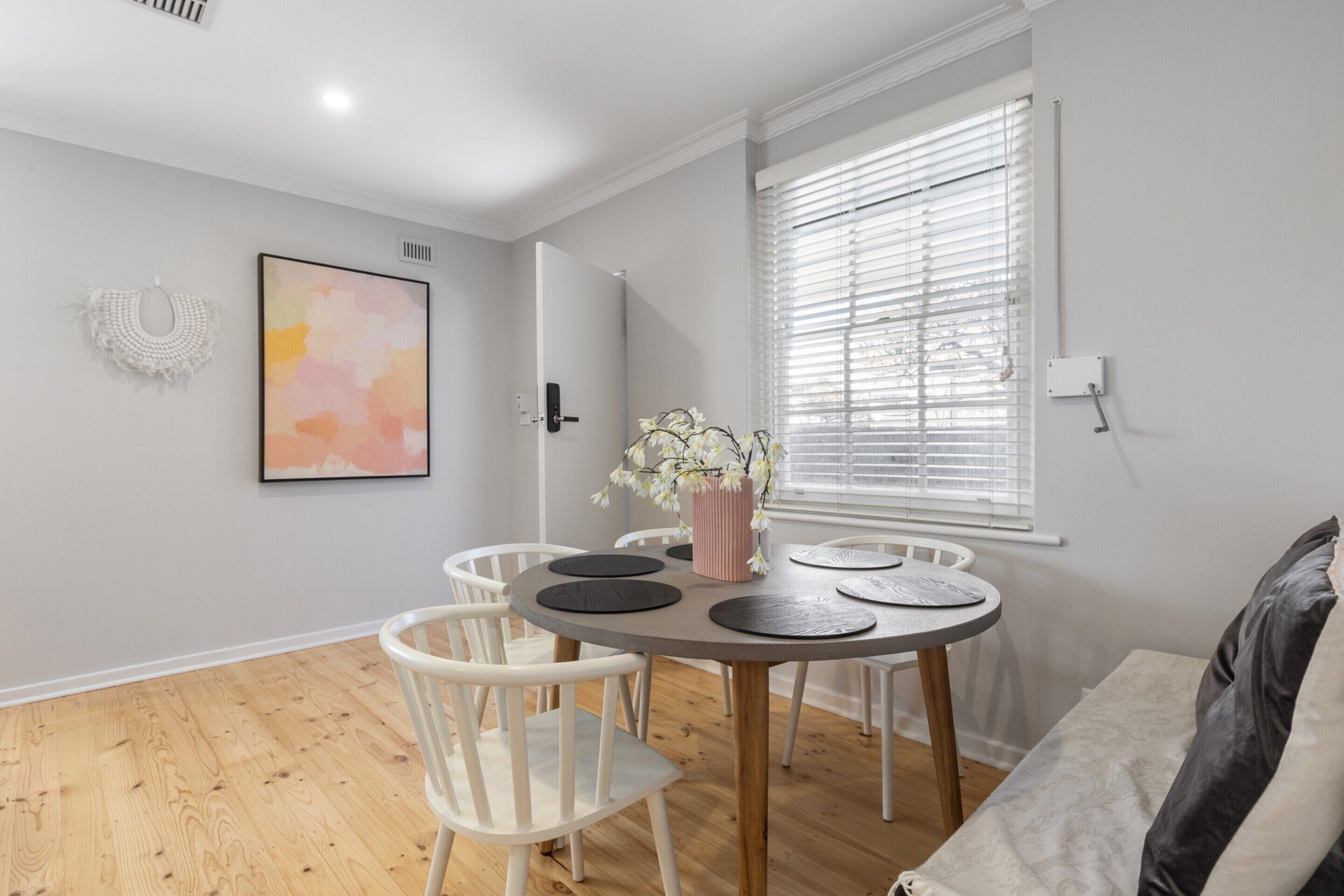Un coin repas avec une table ronde, des chaises blanches et un vase rempli de fleurs.
