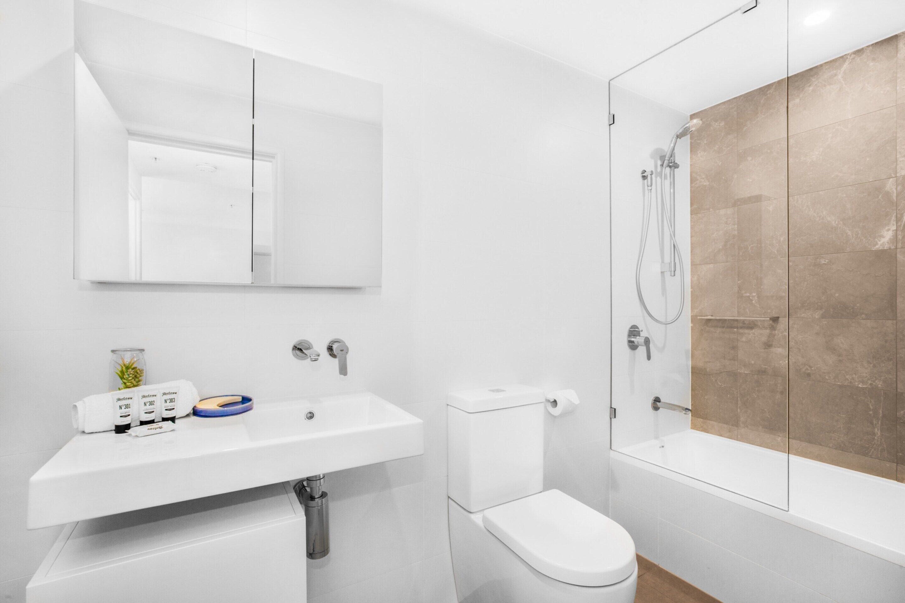 A modern bathroom with a white sink, toilet, and glass-enclosed shower.