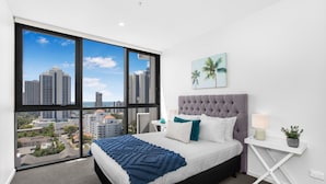 A modern bedroom with a large window, a tufted headboard, and a city view. - 2-bed Beach Apartment With Pool, Parking & Balcony (Gold Coast)