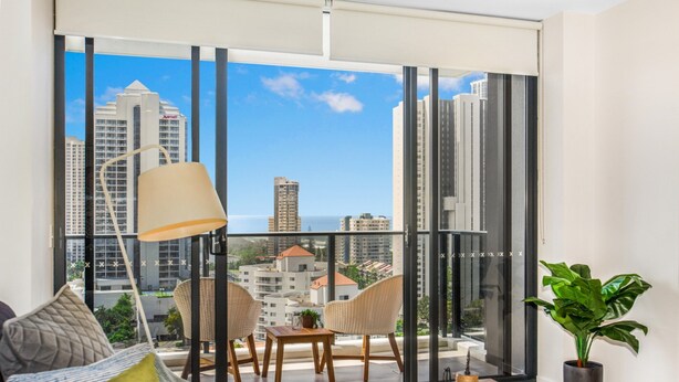 A modern living room with a large window, a sofa, two chairs, a table, and a potted plant. - 2-bed Beach Apartment With Pool, Parking & Balcony (Gold Coast)