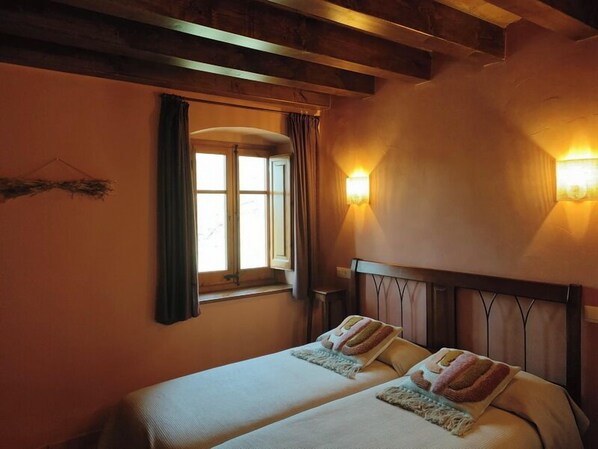 A double bed with a wooden headboard, a window with curtains, and wall-mounted lights. - Casa Serra de Dalt (Lladurs)