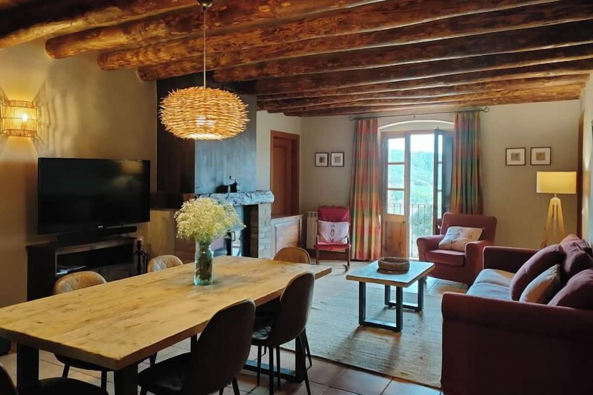 Een gezellige woonkamer met een houten plafond, een open haard, een televisie en een eethoek met een tafel en stoelen.