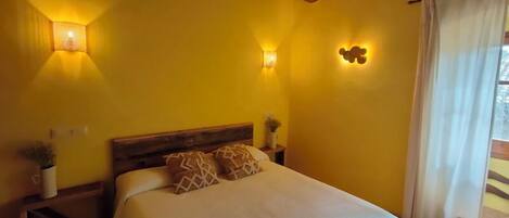 A bedroom with a wooden ceiling, a bed with a white cover, two bedside tables with lamps, and a window with curtains.