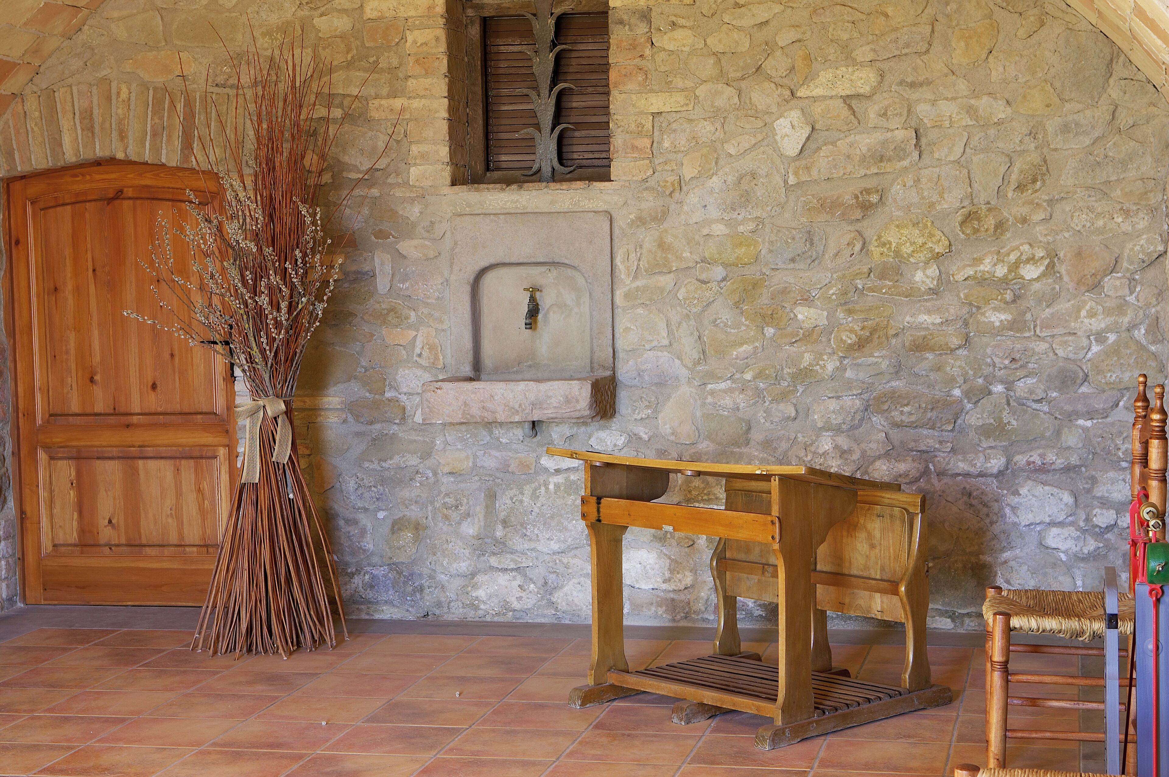 Una habitación rústica con pared de piedra, puerta de madera, una pequeña mesa de madera y una silla.