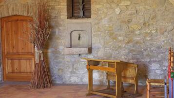Una habitación rústica con pared de piedra, puerta de madera, una pequeña mesa de madera y una silla.