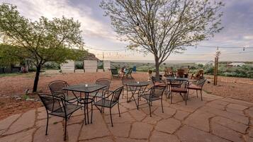 Eine Terrasse im Freien mit Tischen und Stühlen, umgeben von Bäumen und Blick auf die Landschaft.