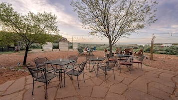 An outdoor patio with tables and chairs, surrounded by trees and a view of the landscape.