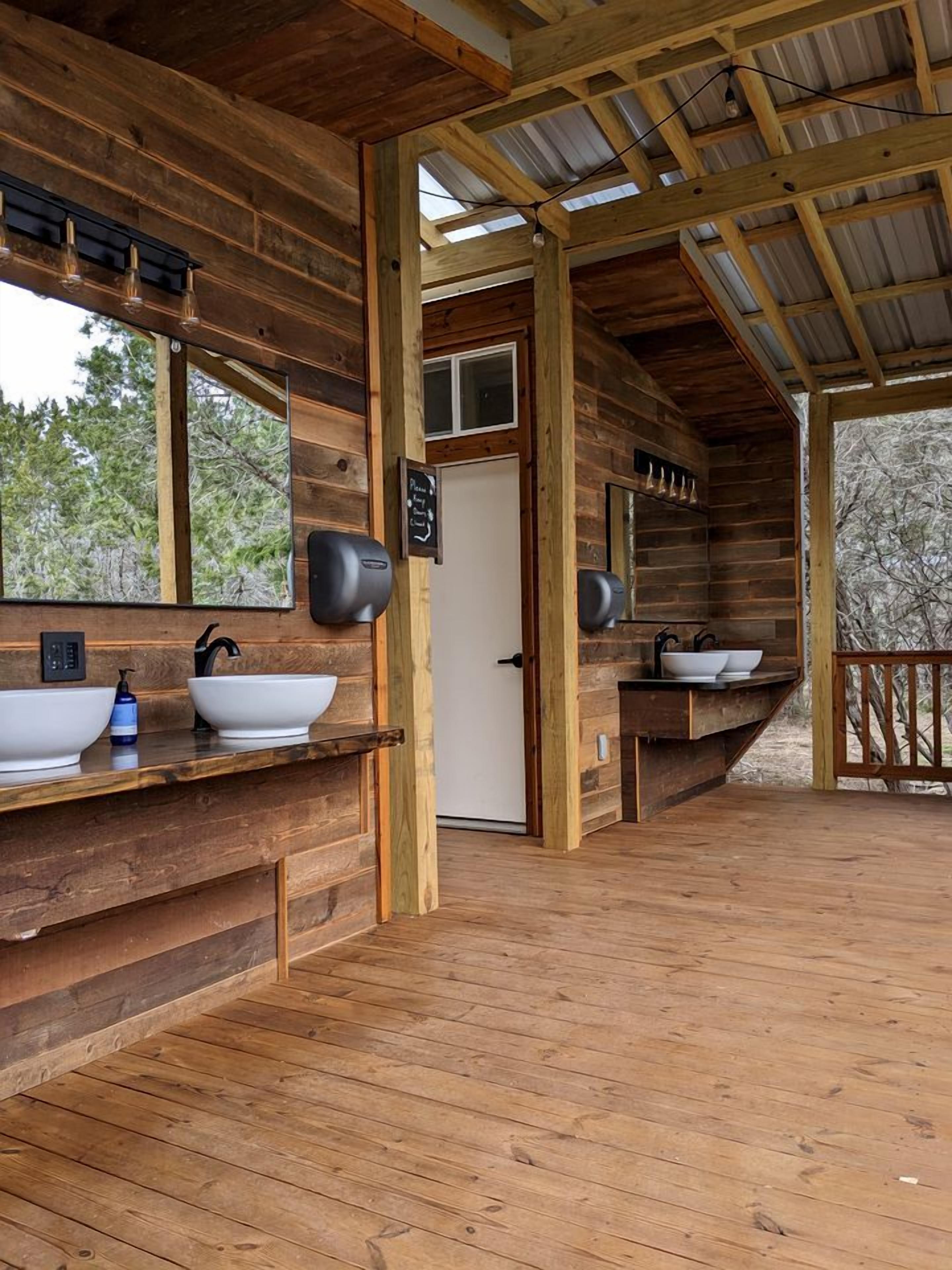 A wooden cabin with a bathroom featuring two sinks, a mirror, and a door.