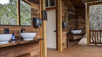 A wooden cabin with a bathroom featuring two sinks, a mirror, and a door.