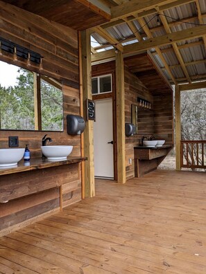A wooden cabin with a bathroom featuring two sinks, a mirror, and a door.
