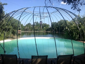 A pool with a metal structure overhead, surrounded by trees and a clear sky.