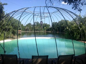 A pool with a metal structure overhead, surrounded by trees and a clear sky.